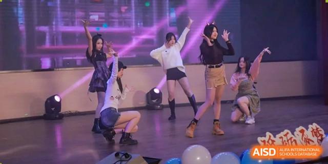 Two female students performing a dance routine on a stage with purple and pink lighting. Chengdu Shishi Tianfu High School International Department.