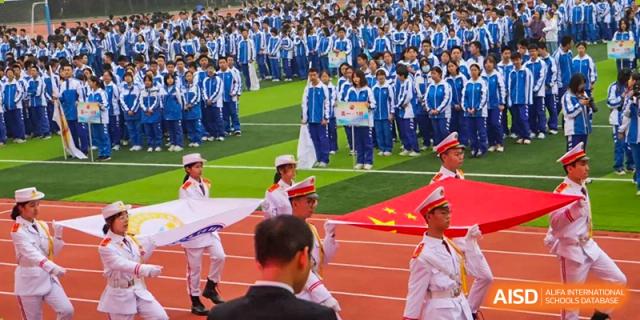 A large group of students in blue and white uniforms holding up banners and a large Chinese flag. Chengdu Shishi Tianfu High School International Department.