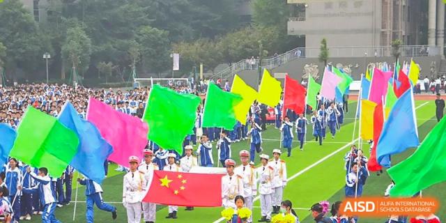 Students marching while holding large green, yellow, and red flags, along with the Chinese flag. Chengdu Shishi Tianfu High School International Department.