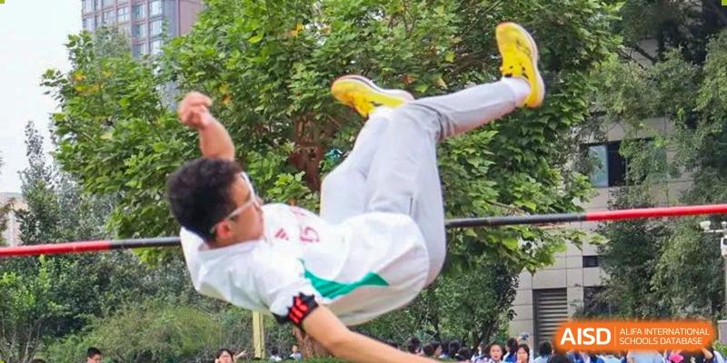 A student in a white uniform performing an athletic flip in mid-air on an outdoor course. Chengdu Shishi Tianfu High School International Department.