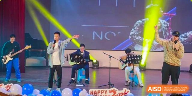 A male student playing a keyboard on a stage with a "Happy" banner. Chengdu Shishi Tianfu High School International Department.