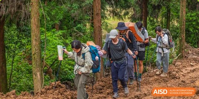 A line of students hiking on a trail in a forest, carrying backpacks. Chengdu Shishi Tianfu High School International Department.