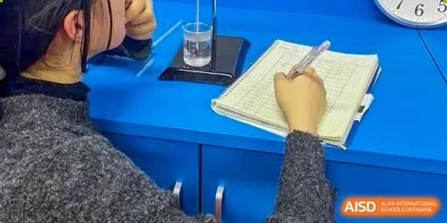 A student taking notes from a notebook and a glass of water on a blue desk at BaiShan AWS High School.