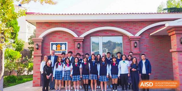 A large group of students in school uniforms posing for a photo in front of a building at BaiShan AWS High School.