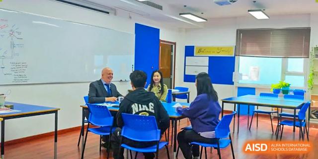 Students and teachers from BaiShan AWS High School participate in a meeting or a classroom discussion around a table.