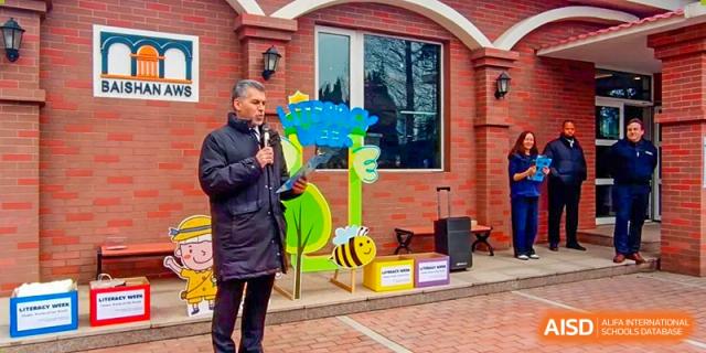 A teacher at BaiShan AWS High School speaks at an outdoor event next to a bee-themed display.