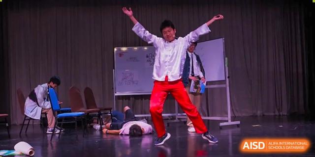 A dramatic street dance performance at a BaiShan AWS High School show, with one dancer lying on the floor.
