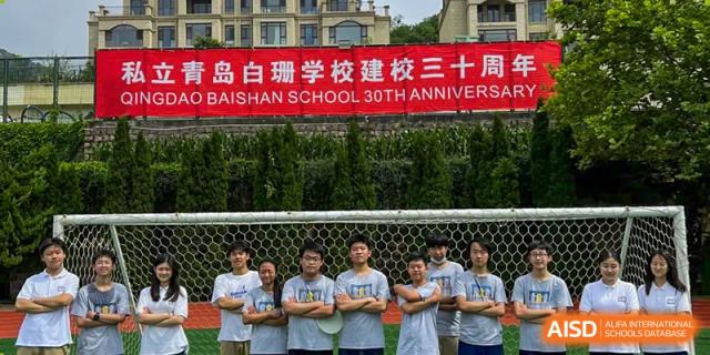 A group of students posing in front of a banner for the BaiShan AWS High School 30th Anniversary.