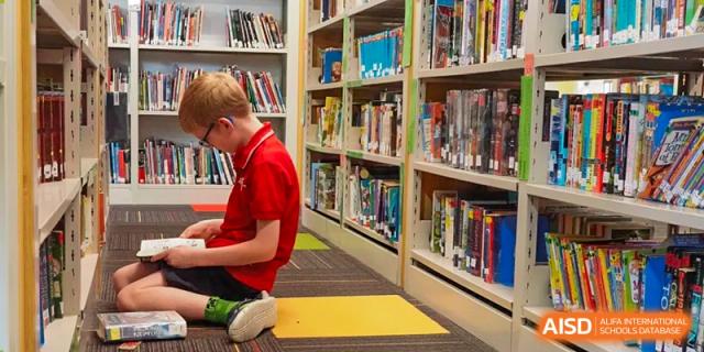 A male student is kneeling on the floor and looking at books on a bookshelf in a library at Chengdu International School.