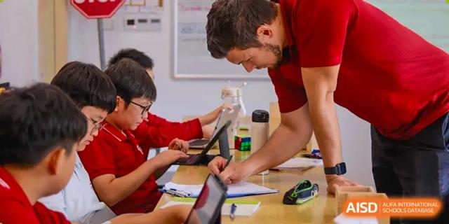 A male teacher is helping a student with a tablet and a workbook at Chengdu International School.