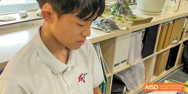 A male student is looking down and writing on a piece of paper at Chengdu International School.