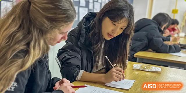 A female student with long hair is looking down and writing on a piece of paper at Chengdu International School.