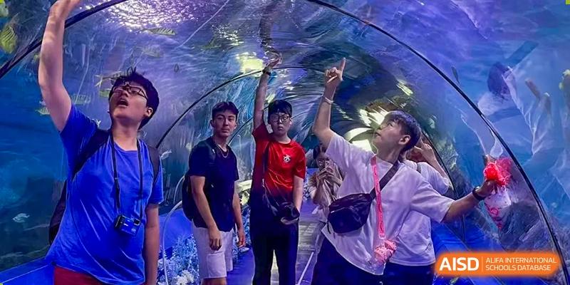 Three students from Chengdu International School are posing for a photo inside a tunnel at an aquarium.