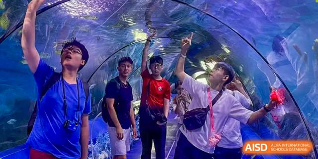 Three students from Chengdu International School are posing for a photo inside a tunnel at an aquarium.