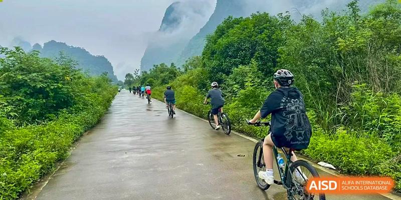 A group of students from Chengdu International School are riding bikes on a path with mountains in the background.
