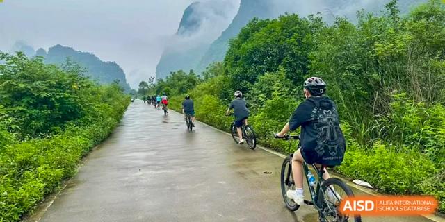 A group of students from Chengdu International School are riding bikes on a path with mountains in the background.