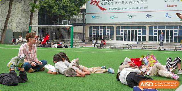 A group of students is relaxing on a grassy sports field at Chengdu International School.