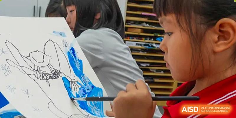 A student's hands are holding a paintbrush and painting on a canvas at Chengdu International School.
