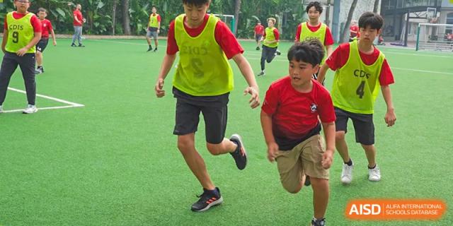 A group of male students in red and yellow vests is participating in a race on a grassy field at Chengdu International School.