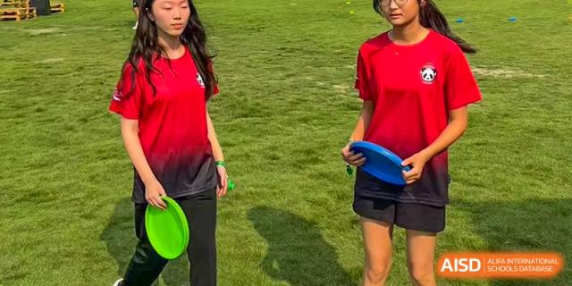 Two students are on a grassy field, one of them holding a blue frisbee at Chengdu International School.