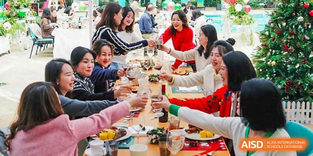 A group of people is sitting at a table with plates of food and drinks, toasting to each other at Chengdu International School.
