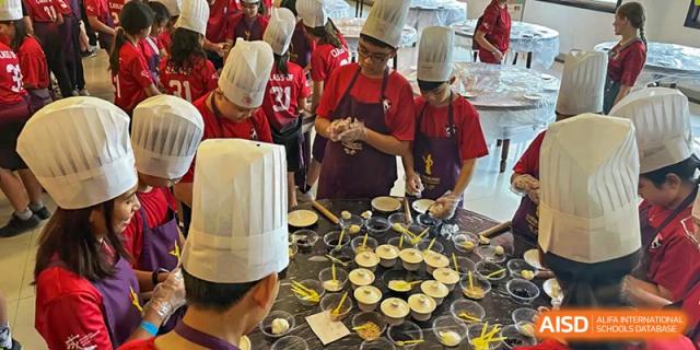 Students in red aprons are cooking with a professional chef at a counter at Chengdu International School.
