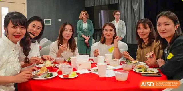 A group of women is sitting at a red table with plates of food and smiling at the camera at Chengdu International School.