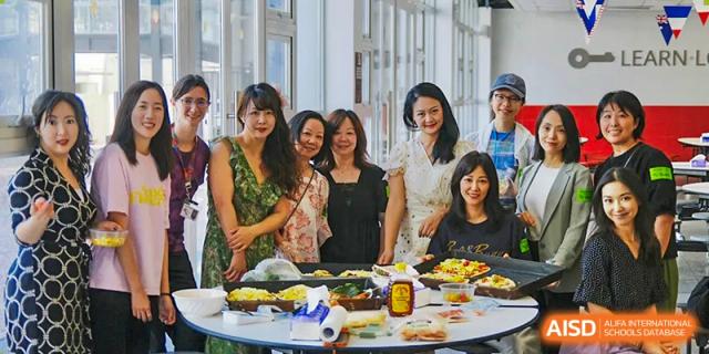 A group of people, including students and staff, is posing for a photo with a variety of food on a table at Chengdu International School.