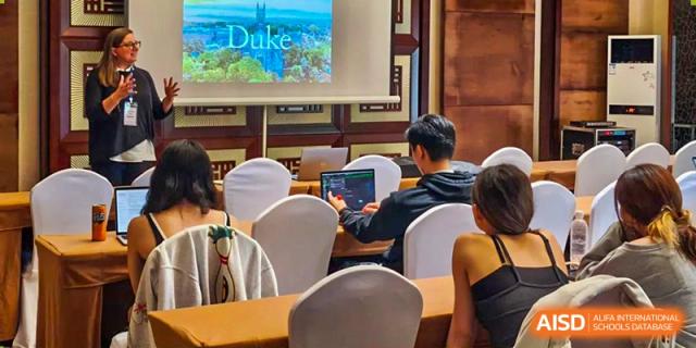 Students at Shanghai American School are using laptops in a classroom with a presentation screen that says "Duke" in the background.