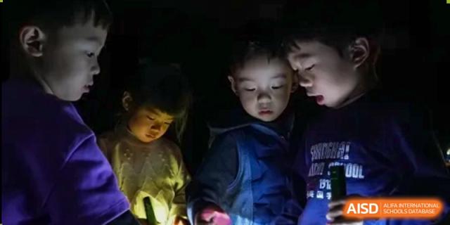 Young students at Shanghai American School are looking at a glowing object in a dark room.