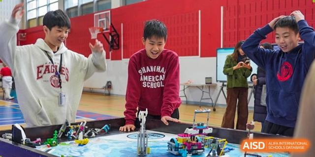 A male student at Shanghai American School is smiling while building with Lego pieces for a robotics competition.