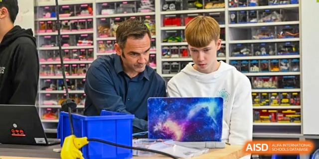 A male student and a teacher at Shanghai American School are looking at a laptop while working on a robotics project.