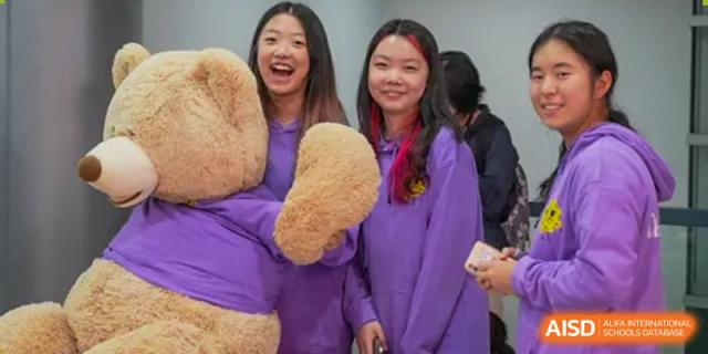 Two female students at Shanghai American School are posing together with a large teddy bear.