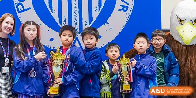 Two young students from Shanghai American School are proudly holding trophies at an awards ceremony.