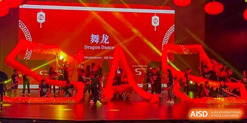 Students at Shanghai American School are performing a "Dragon Dance" on a stage during a cultural event.