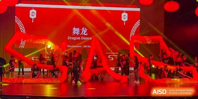 Students at Shanghai American School are performing a "Dragon Dance" on a stage during a cultural event.