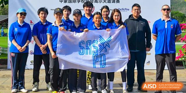 A group of students from Shanghai American School is holding up a banner that says "SAS PD" at an outdoor event.