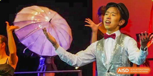 A student from Shanghai American School is on stage, holding a large white umbrella during a performance.