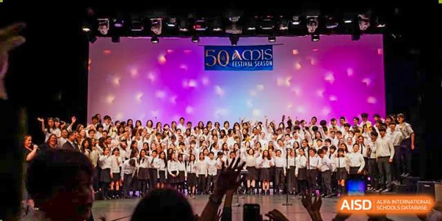 A large group of students from Shanghai American School is waving from a stage at a festival.