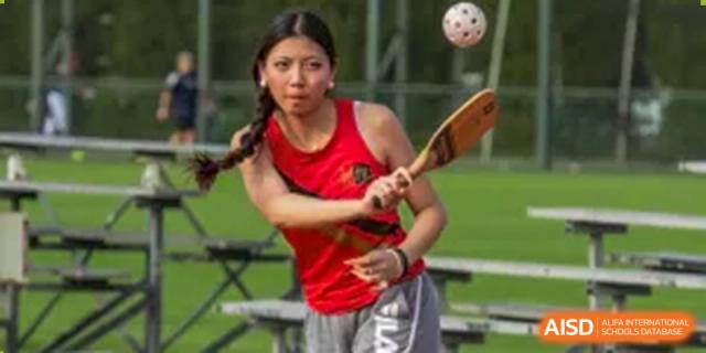 A female student from Shanghai American School is playing field hockey with a wooden stick.