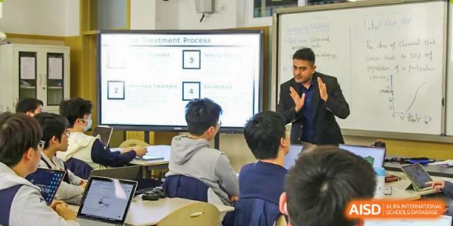 Male teacher standing and giving a presentation to a class of students seated at desks, Beijing Etown Academy International Department