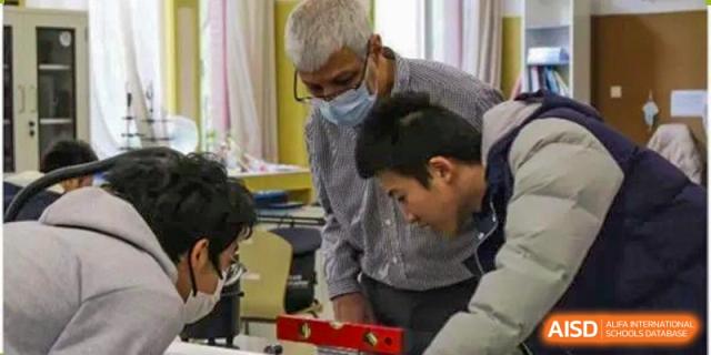 Two men working together, one inspecting a project with a red level tool, possibly during a design or engineering activity, Beijing Etown Academy International Department