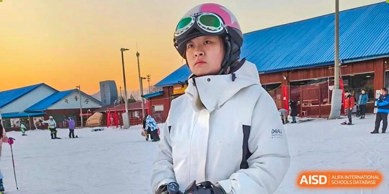 Woman in a white winter jacket and pink ski goggles outdoors in a snowy landscape, Beijing Etown Academy International Department