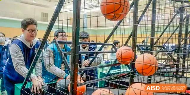 Students looking through the metal bars of a sports cage or enclosure containing basketballs, Beijing Etown Academy International Department