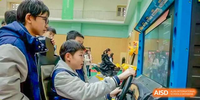 Young boy concentrating while sitting and holding a steering wheel, possibly on a simulator or ride, Beijing Etown Academy International Department