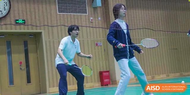 Two young people playing badminton on a green court in an indoor gym, Beijing Etown Academy International Department