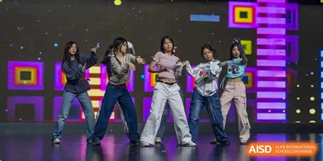 Group of young people in casual attire performing a dance routine on a dark stage with colorful lighting, Beijing Etown Academy International Department