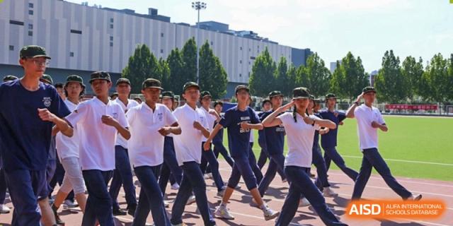 Students in white shirts and navy pants marching or doing calisthenics outdoors on a running track, Beijing Etown Academy International Department