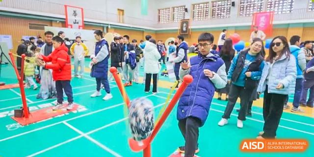 A person playing an outdoor game or activity, holding a large slingshot device with a ball, Beijing Etown Academy International Department