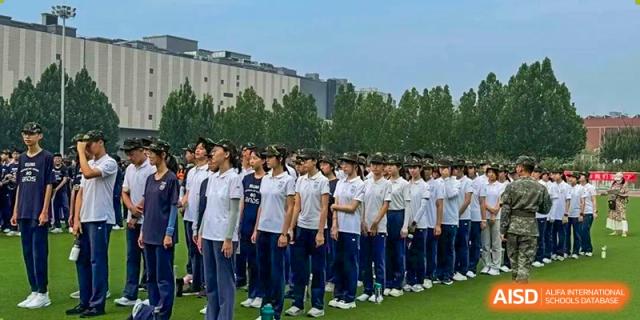 Large group of students in matching white shirts and dark pants standing in neat formation on a grassy field, Beijing Etown Academy International Department